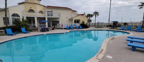 A swimming pool with blue lounge chairs and a building with a balcony in the background.