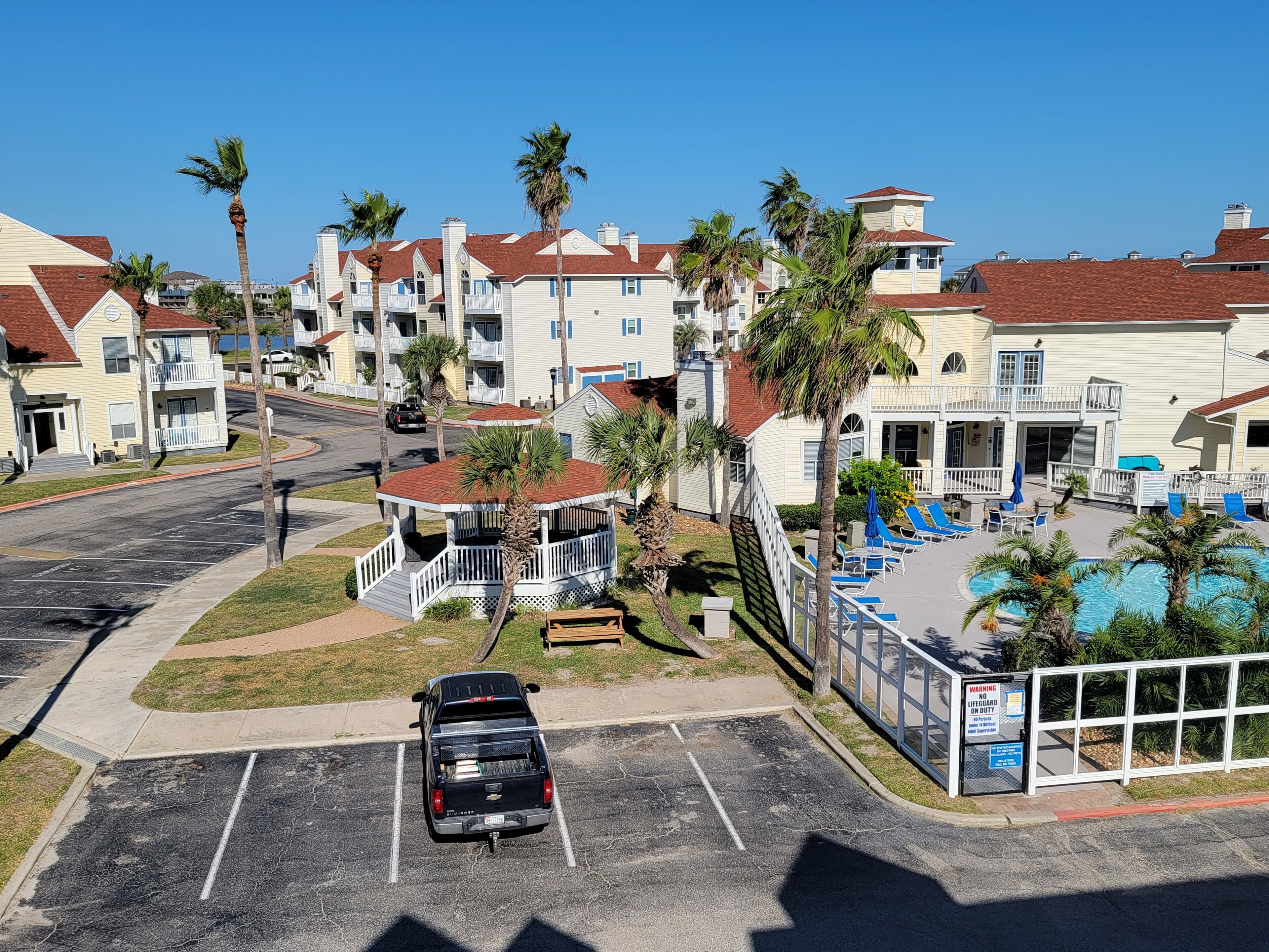 A residential area with a parking lot, a small gazebo, and a pool area with lounge chairs.