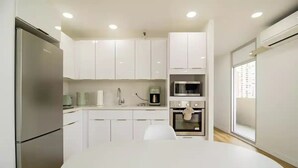 Una cocina moderna con armarios blancos, electrodomésticos de acero inoxidable y una mesa redonda blanca.