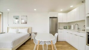 Una habitación de hotel moderna con cama, una mesa de comedor con sillas, una kitchenette y un refrigerador.