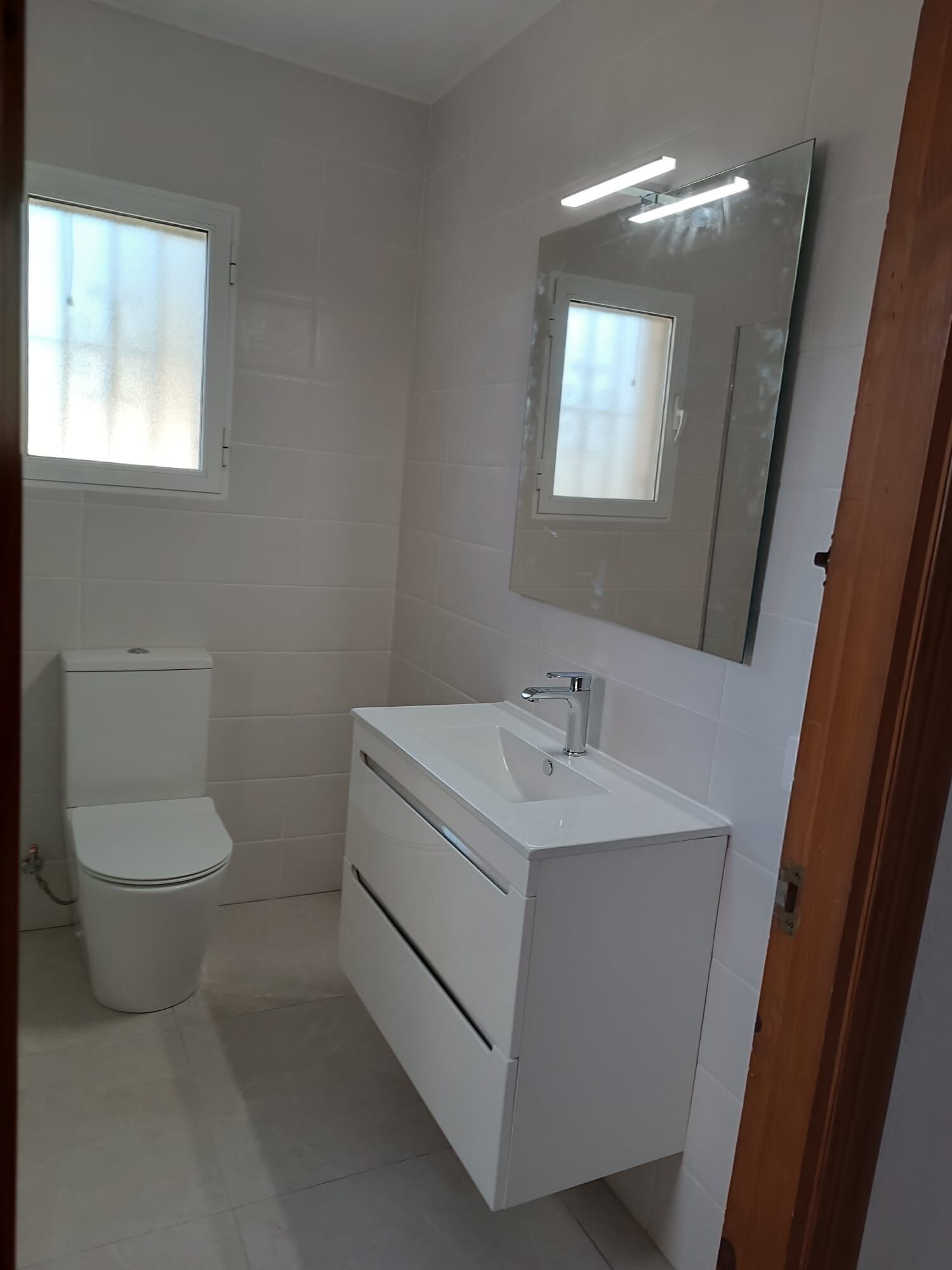 Une petite salle de bain propre, avec des éléments d’aménagement blancs, des toilettes, un lavabo et un miroir.