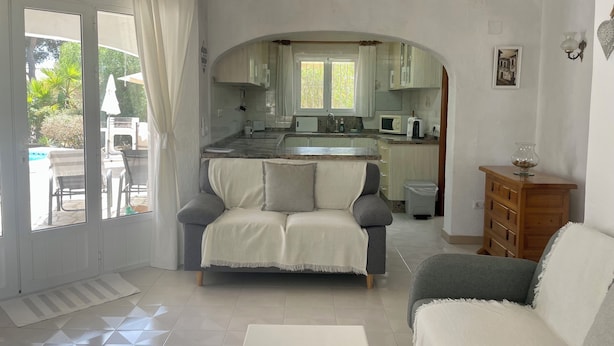 Ein Wohnzimmer mit einer Couch, einem Couchtisch und Blick auf eine Küche durch einen Bogen.