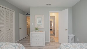 Une chambre avec deux lits, une commode, un miroir et un couloir menant à la salle de bain.