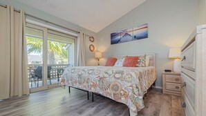 Ein Schlafzimmer mit Bett, Nachttisch, Kommode, einem Fenster mit Vorhängen und einem Wandbild.