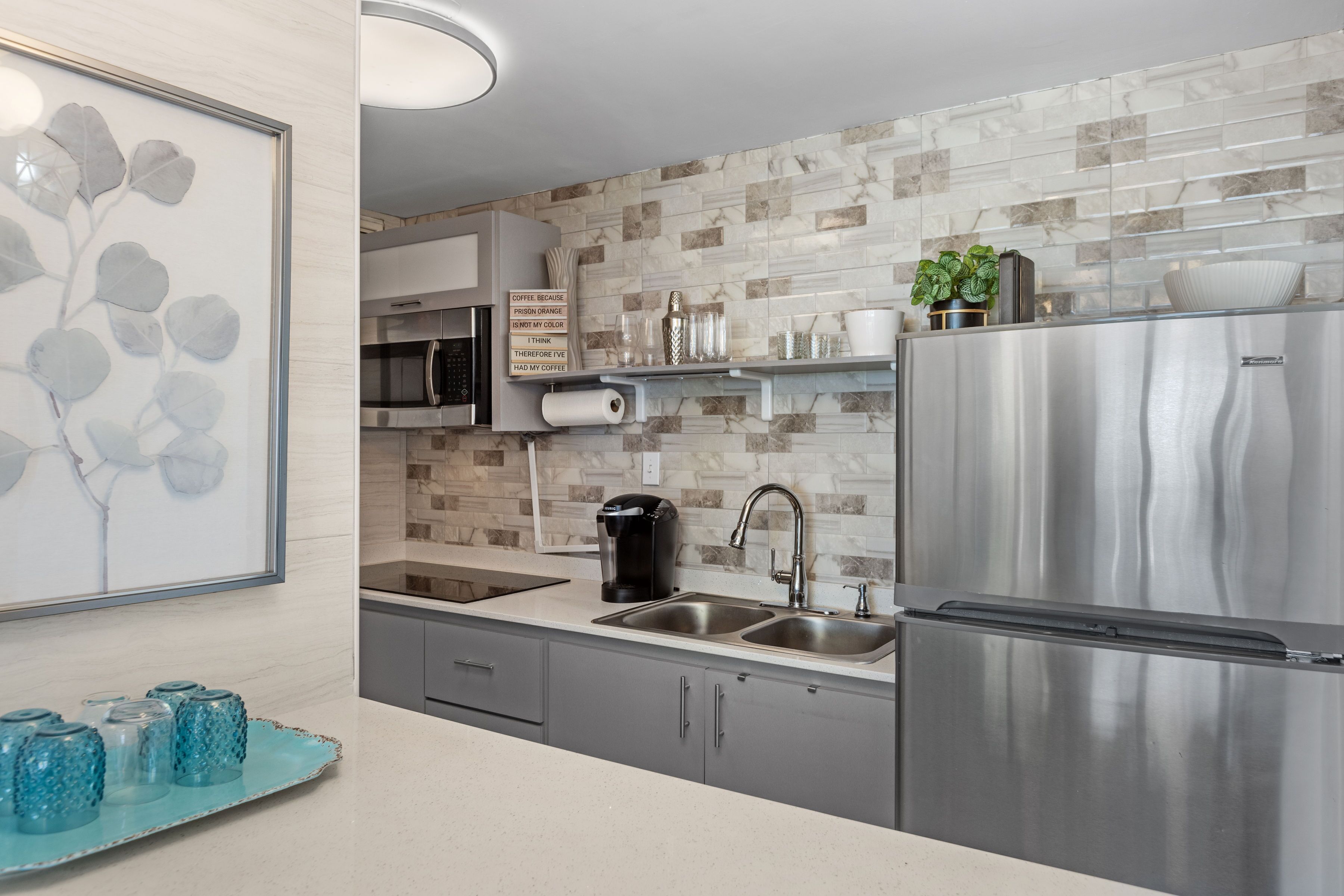 Uma cozinha moderna com eletrodomésticos de aço inoxidável, painel de fundo de mármore e uma bandeja decorativa azul.
