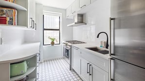 A modern kitchen with white cabinets, a stainless steel refrigerator, and a tiled floor. - Classy 2BR/1,5BA Boutique at Flushing! (Queens)