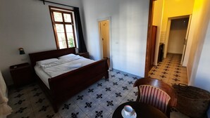 A bedroom with a bed, a nightstand, a window with curtains, a door, and a tiled floor. - Haifa Vintage Rooms (Haifa)