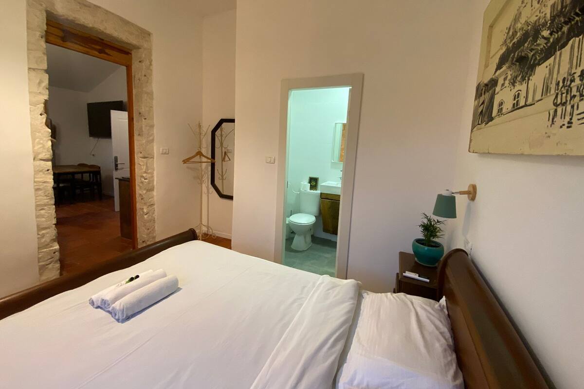 A bedroom with a large bed, a wooden headboard, a bedside table with a lamp, and a painting on the wall.