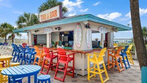 Un bar de style tiki avec des chaises et des tables aux couleurs vives, une enseigne et un panneau affichant le menu.