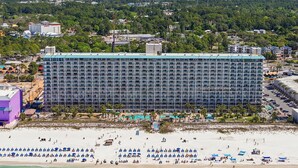 Un grand hôtel avec un bâtiment long et rectangulaire, une plage dotée de nombreux parasols et de chaises longues, et une vue dégagée sur l’océan.