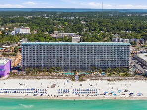 Un hotel grande con un edificio largo y rectangular, una playa con numerosas sombrillas y tumbonas, y una vista despejada del océano.