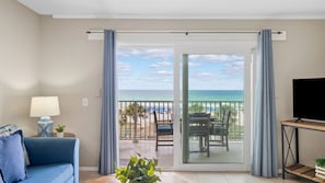 Una habitación con balcón, sofá, televisión y vista a la playa.