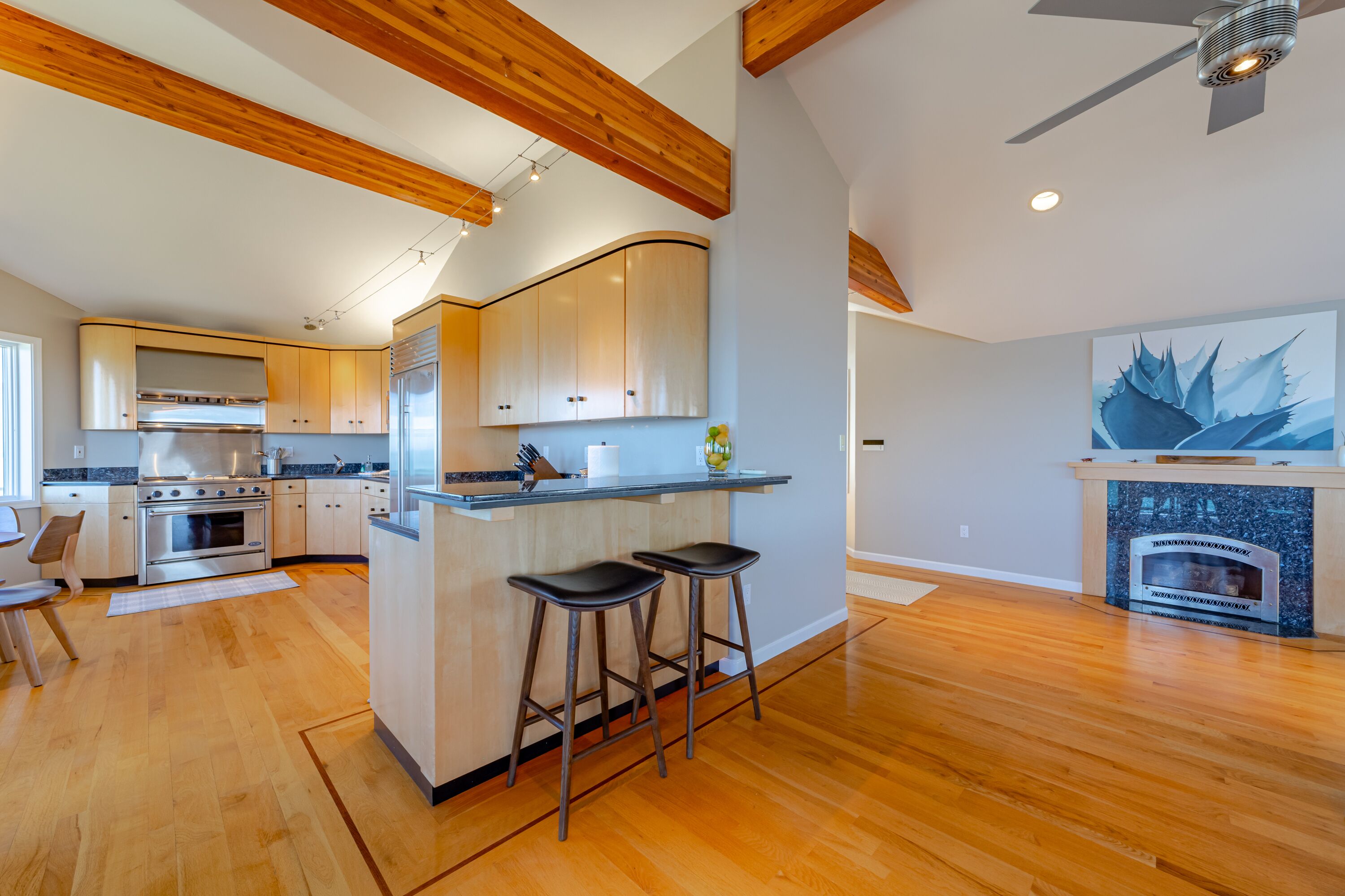 A modern kitchen with wooden beams, a central island with stools, and a built-in oven.