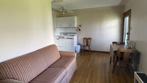 En kompakt opholdsstue med sofa, spisebord med stole, et tekøkken og en loftsvift.