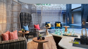 A modern lounge area with wicker furniture, a round wooden table, and a view of a water feature. - Marriott's Bali Nusa Dua Terrace (Nusa Dua)