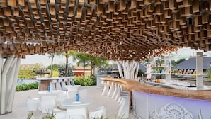 An outdoor seating area with white tables and chairs, a wooden ceiling structure, and a bar area with a decorative screen. - Marriott's Bali Nusa Dua Terrace (Nusa Dua)