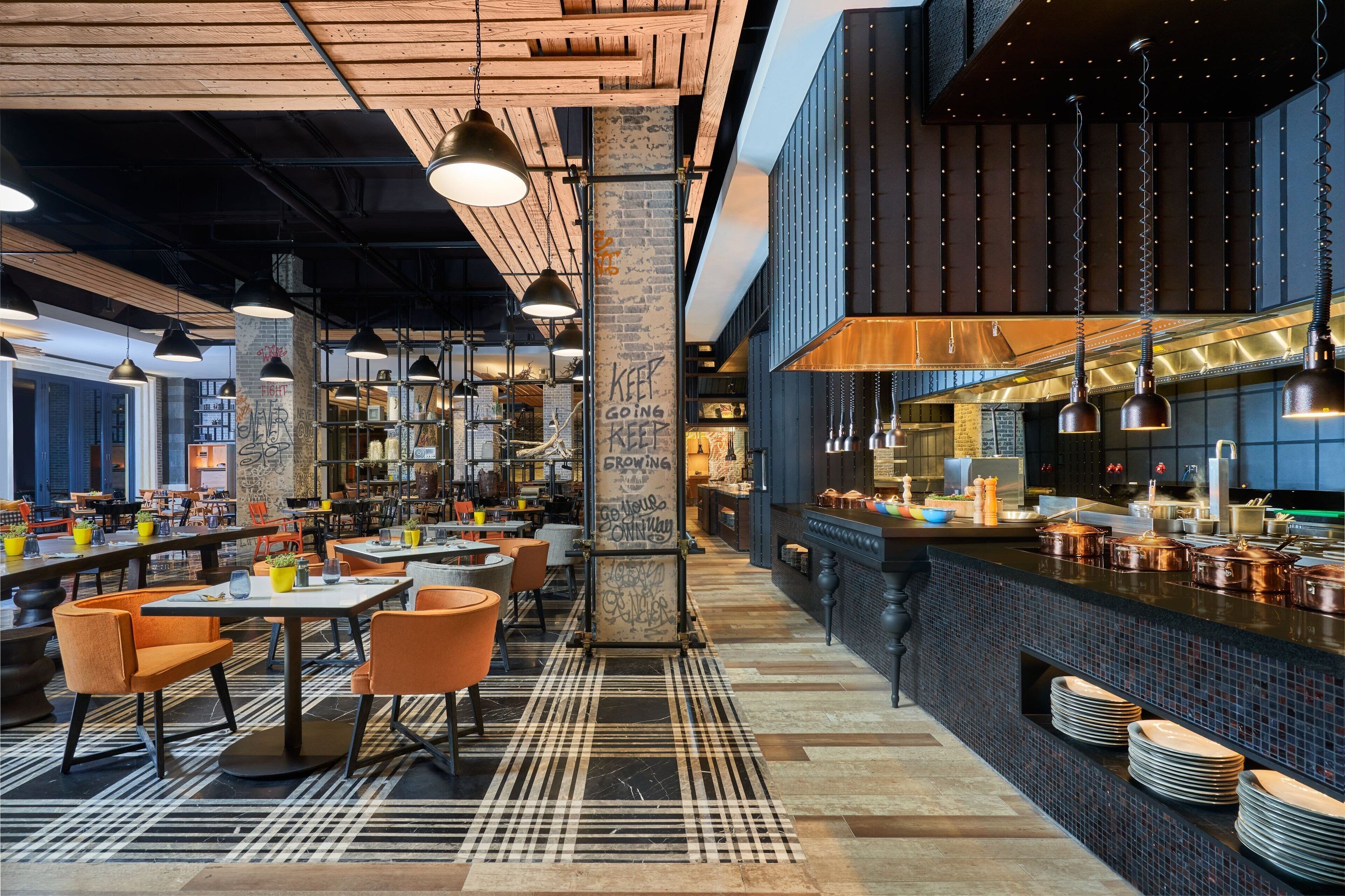 A modern restaurant with exposed brick walls, wooden ceiling beams, and a mix of seating arrangements including tables and chairs.