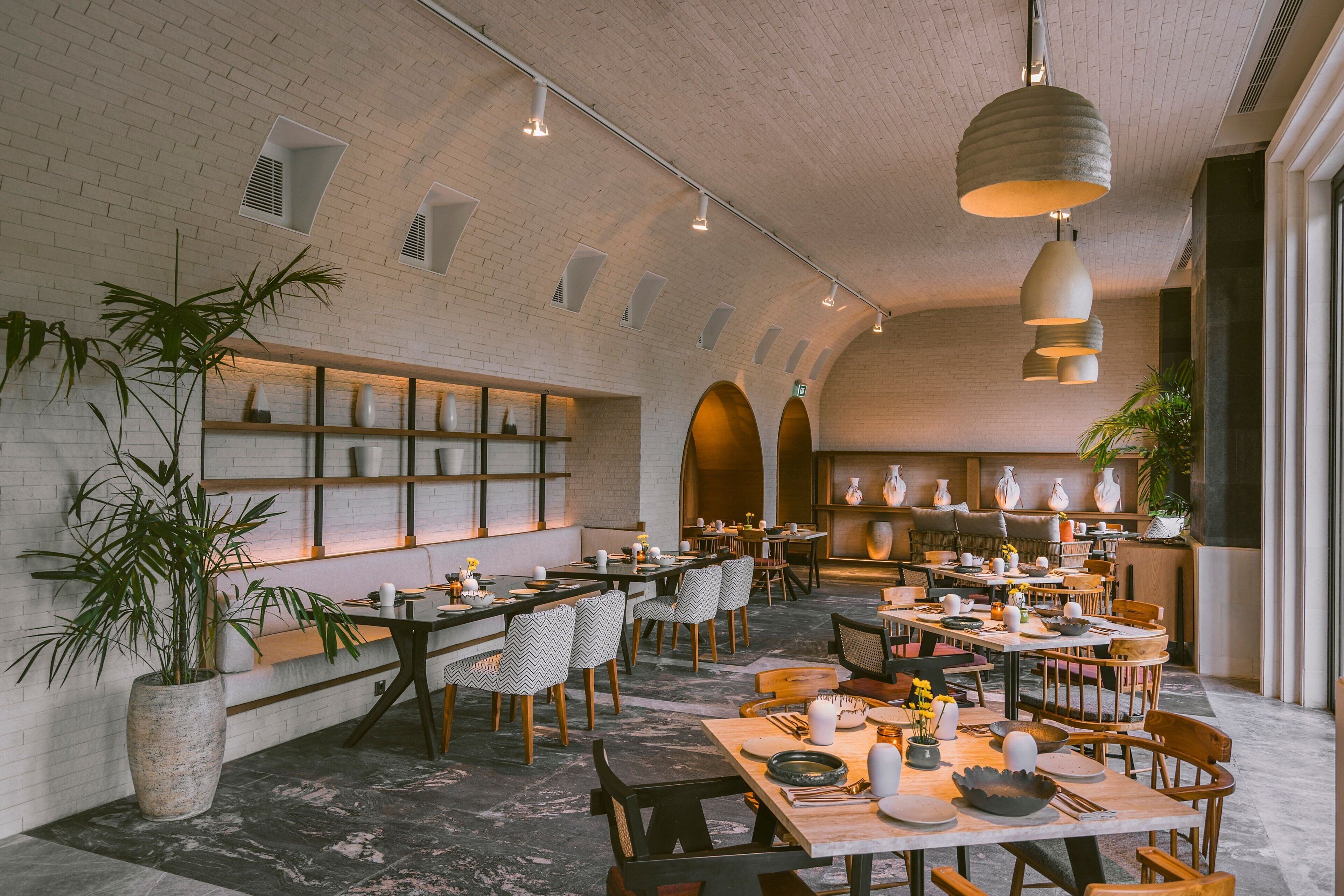 Un restaurante espacioso con techos altos, paredes de ladrillo visto y diferentes opciones de mesas.