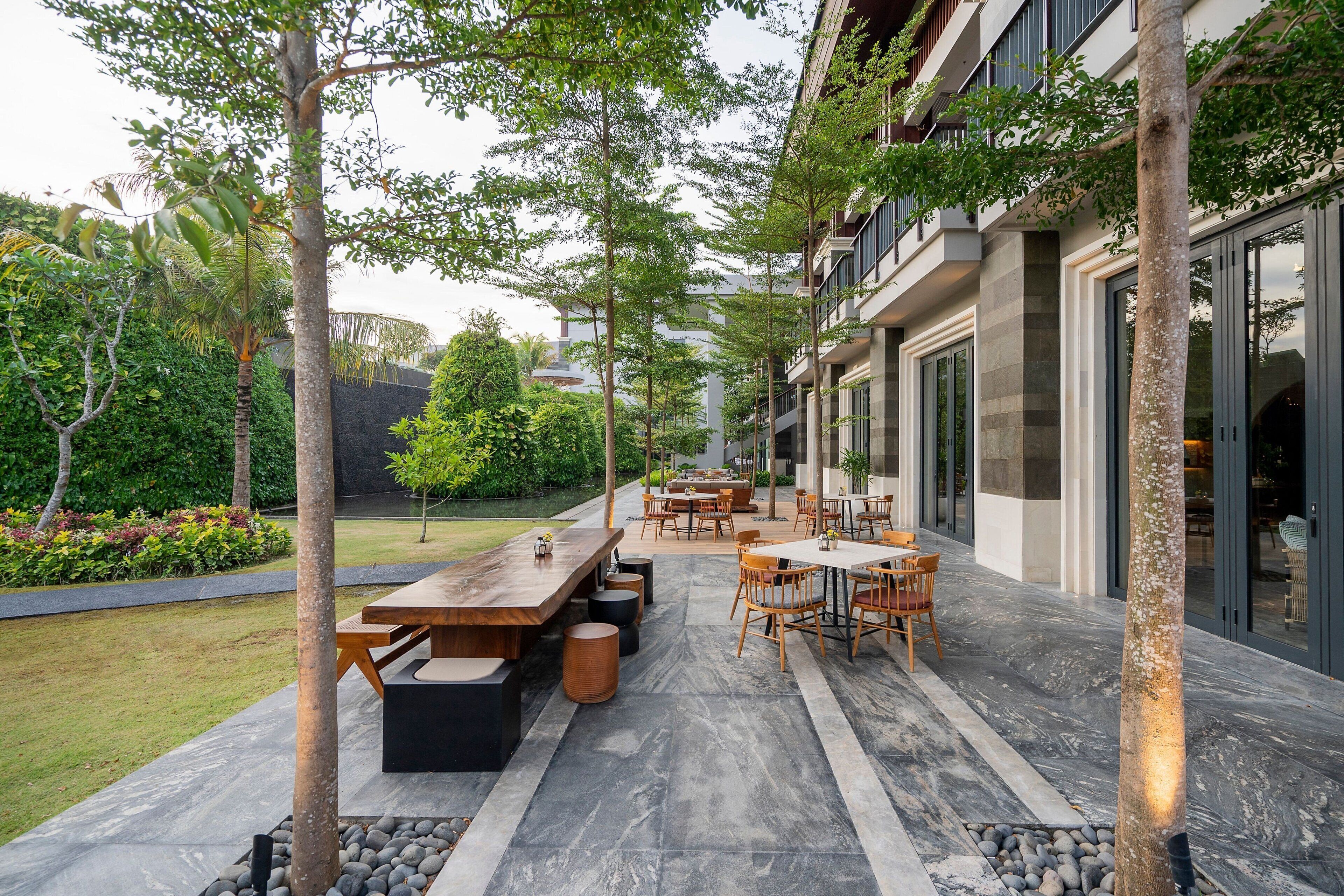 An outdoor patio area with tables and chairs, surrounded by trees and a garden.