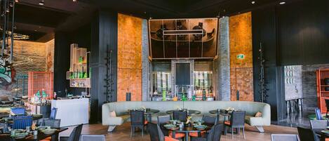 A modern restaurant with a central seating area, a bar, and a high ceiling with industrial lighting.