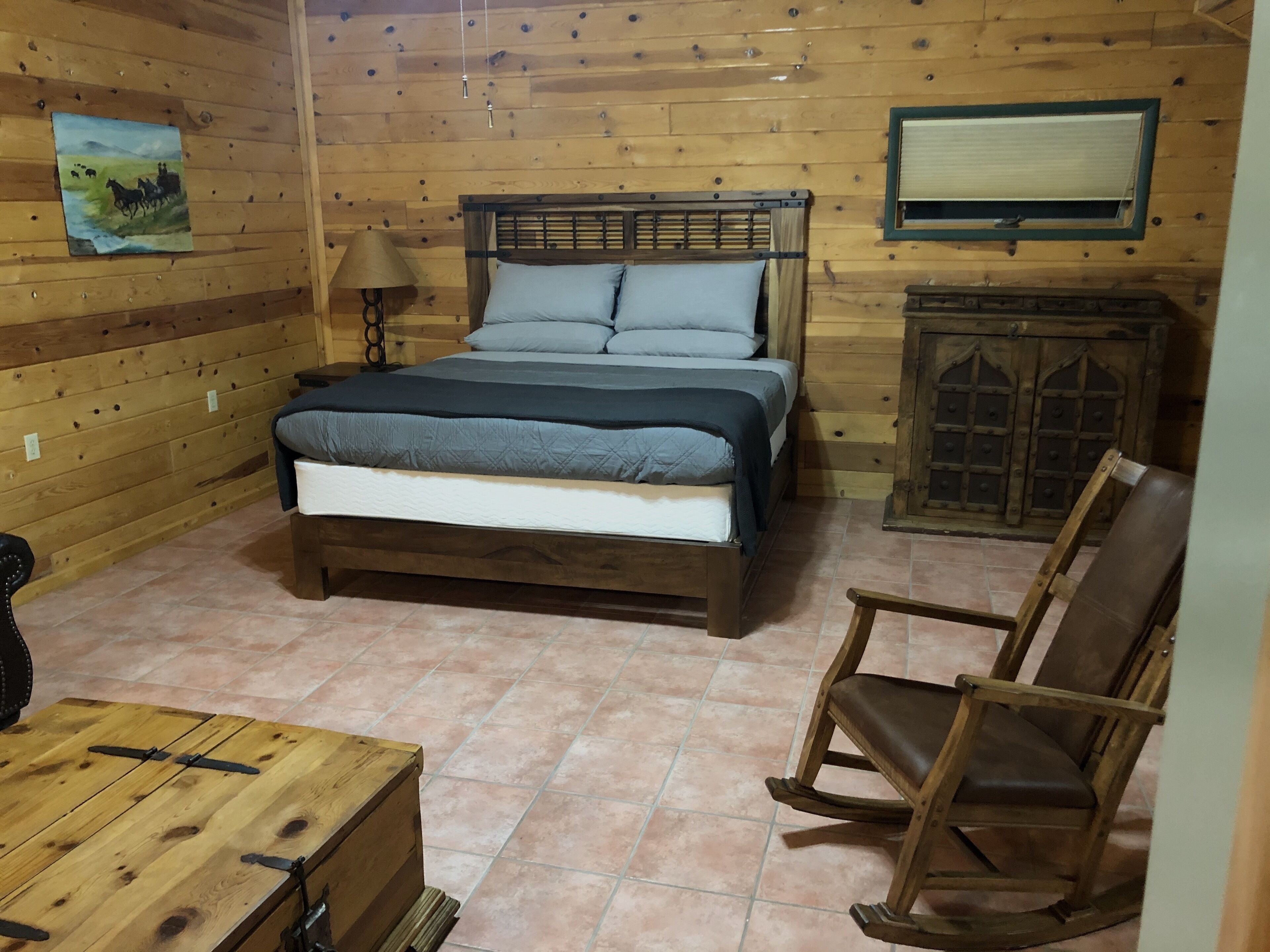 Een houten kamer met een bed, een stoel, een tafel en een kast.