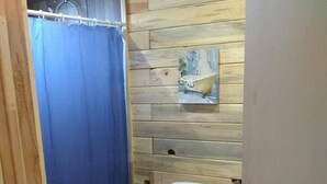 A small bathroom with a wooden wall, a blue shower curtain, a white toilet, and a small trash bin. - Cabanas Ejido Santa Rosa Kilo78  Codigo 22766 (Santa Rosa)