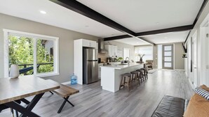 A modern kitchen with a central island, large windows, and a dining area with a bench.