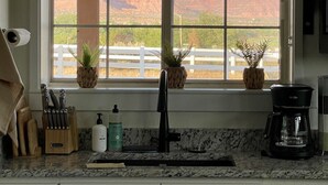 A kitchen with a window view of a red rock landscape, a coffee maker, and a knife block. - Modern Studio with Kitchen, Washer/Dryer, Fire Pit, Grill, & Red Rock Views! (Kanab)