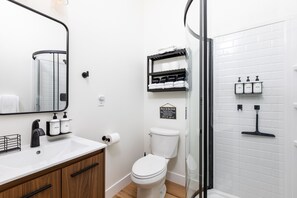 A modern bathroom with a white sink, black faucet, and a toilet. There are shelves with toiletries and a sign on the wall. - Modern Studio with Kitchen, Washer/Dryer, Fire Pit, Grill, & Red Rock Views! (Kanab)