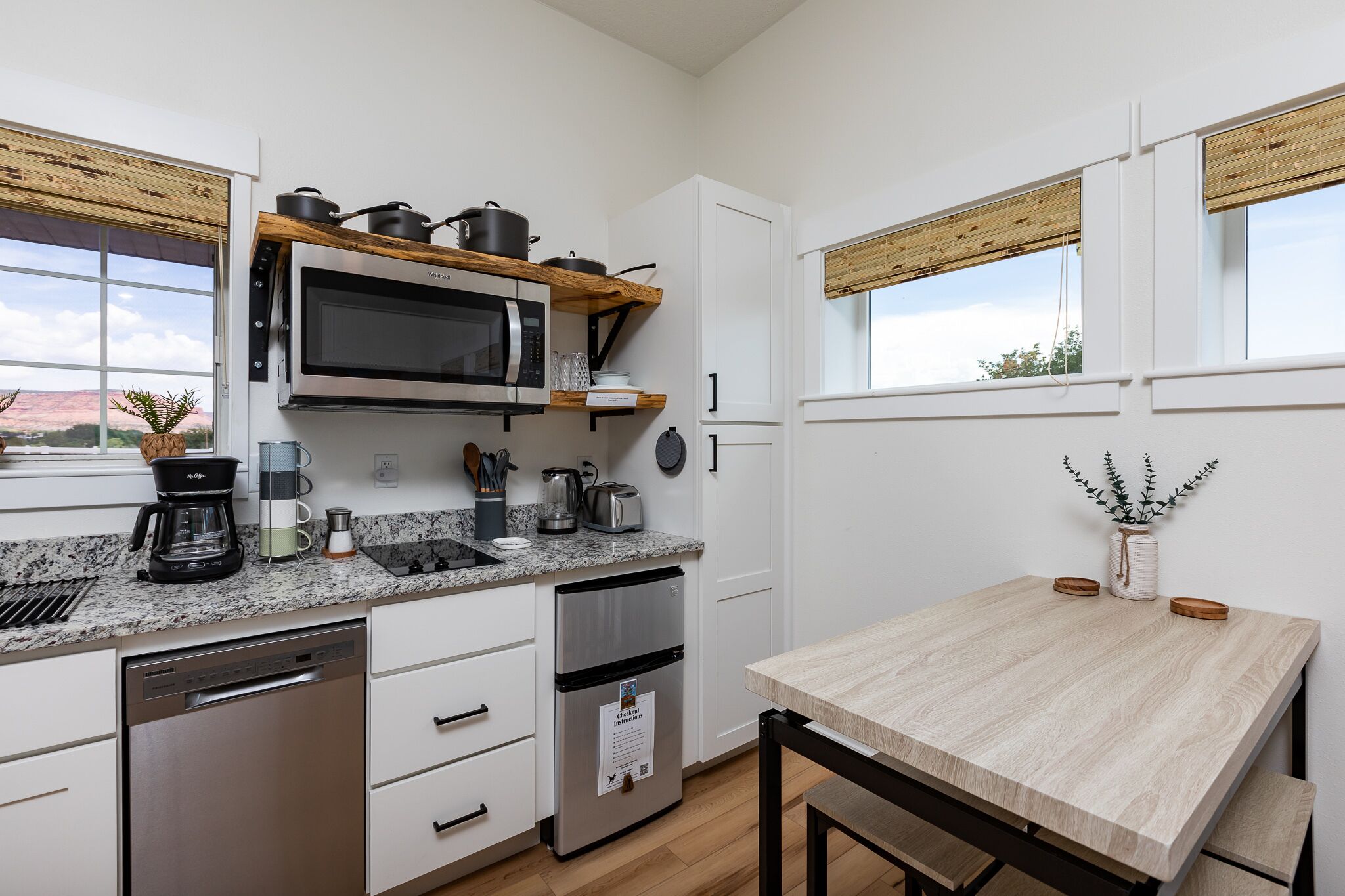 Een moderne keuken met een ingebouwde magnetron, roestvrijstalen apparatuur, een koffiezetapparaat en een houten tafel.