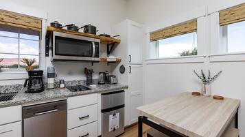 Een moderne keuken met een ingebouwde magnetron, roestvrijstalen apparatuur, een koffiezetapparaat en een houten tafel.