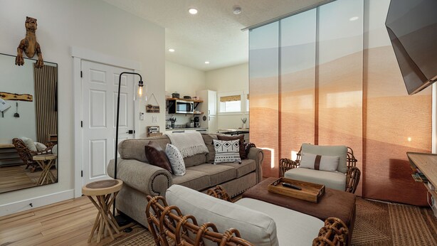 A modern living room with a sofa, chairs, and a dining table. There is a kitchen in the background with a microwave and cabinets. - Modern Studio with Kitchen, Washer/Dryer, Fire Pit, Grill, & Red Rock Views! (Kanab)