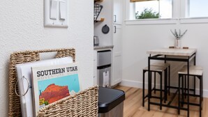 A kitchen with white cabinets, a black countertop, and a wooden table with bar stools. - Modern Studio with Kitchen, Washer/Dryer, Fire Pit, Grill, & Red Rock Views! (Kanab)