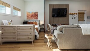 A modern bedroom with a bed, a sofa, a wooden dresser, and a television mounted on the wall. - Modern Studio with Kitchen, Washer/Dryer, Fire Pit, Grill, & Red Rock Views! (Kanab)