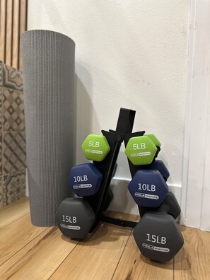A set of adjustable dumbbells with weights ranging from 5lb to 15lb, placed on a wooden floor next to a grey cylindrical object. - Modern Studio with Kitchen, Washer/Dryer, Fire Pit, Grill, & Red Rock Views! (Kanab)