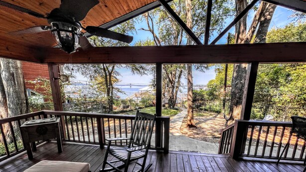 A wooden deck with a rocking chair and a cushioned bench, overlooking a forested area and a body of water.