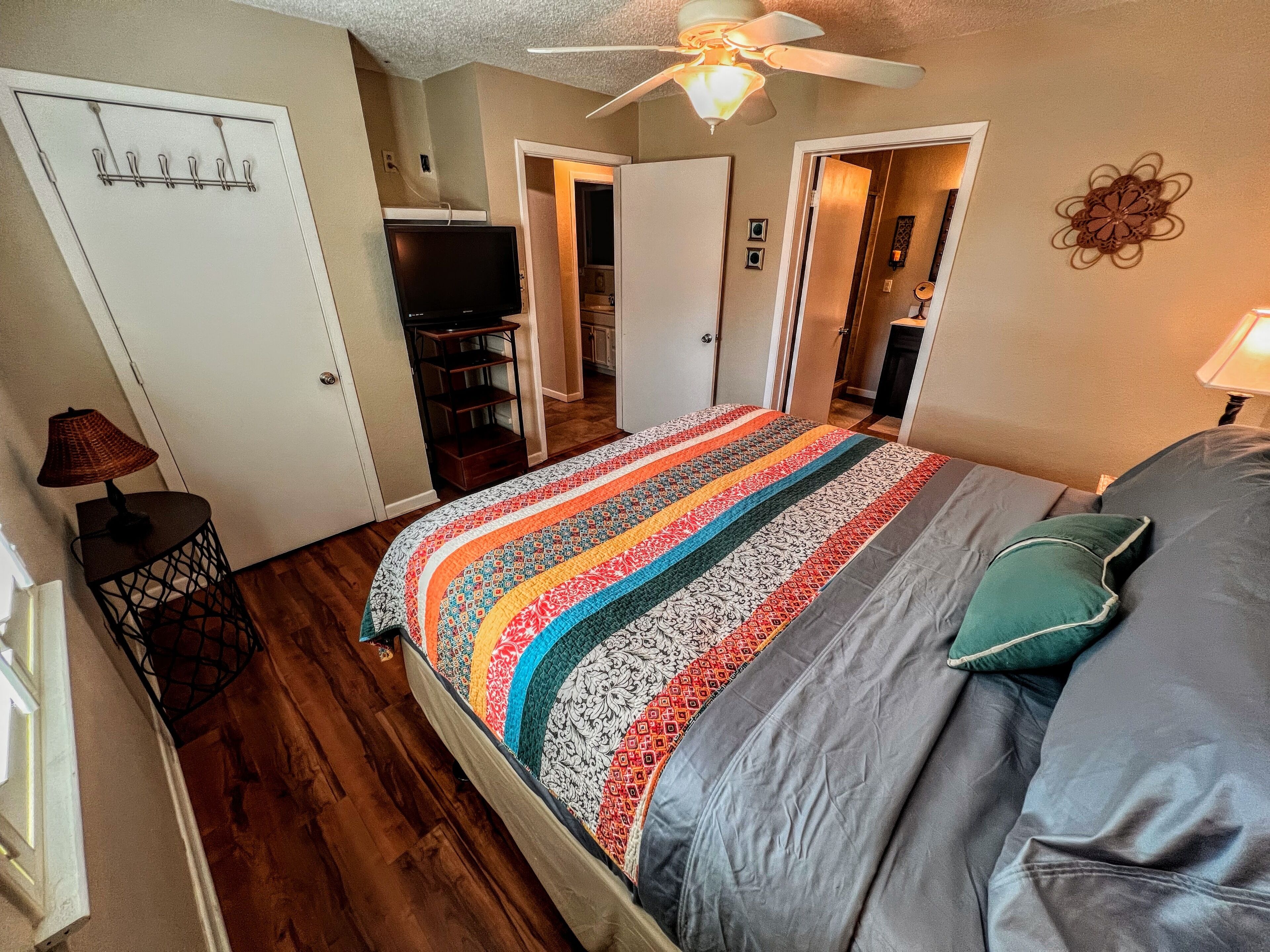 A bedroom with a bed, a ceiling fan, a TV, and a door leading to a bathroom.