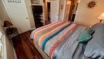 A bedroom with a bed, a ceiling fan, a TV, and a door leading to a bathroom.