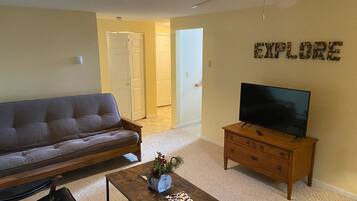 Ein Wohnzimmer mit einer Couch, einem Couchtisch mit einer Pflanze, einem Fernseher auf einem Holzständer und einem Deckenventilator.