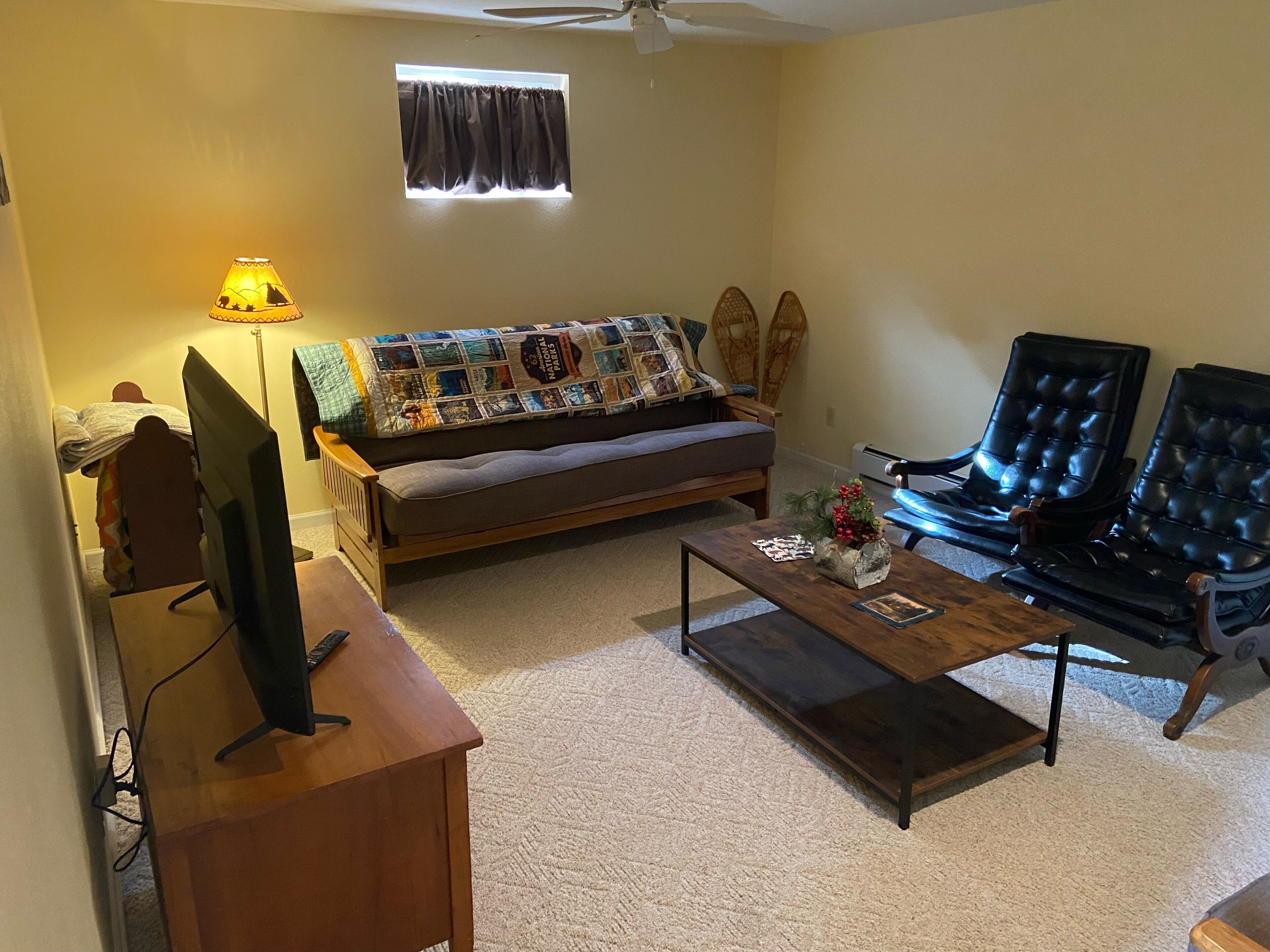 Una sala de estar con un sofá, dos sillones, una mesa de centro, un televisor sobre un mueble bajo y una ventana con cortinas.