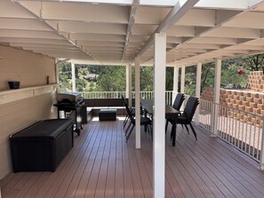 A covered patio with a grill, seating, and a view of the backyard. - Black Bear Ridge Vacation Home (Raton)