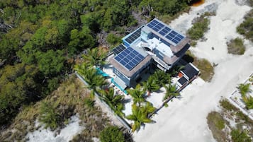 Un edificio grande con varios paneles solares en el techo, rodeado de palmeras y una zona arenosa.