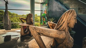 A sculpture of a woman in a relaxed pose, a wooden table, and a colorful mural in a room with large windows. - Costa Nube (Caye Caulker)