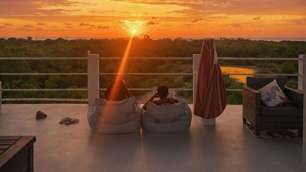 A sunset view from a balcony with bean bags, a chair, and a hanging cloth. - Costa Nube (Caye Caulker)