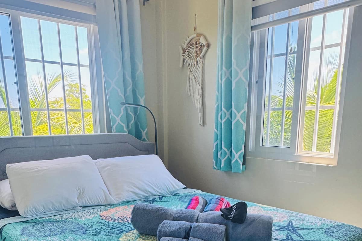 A bed with a blue and green ocean-themed bedspread, white pillows, and a dreamcatcher on the wall.