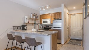 A modern kitchen with a central island, bar stools, wooden cabinets, a microwave, and a refrigerator. - Ground Floor Creekside Condo - great for hiking and biking! (Silver Star Mountain)
