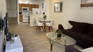 A modern living room with a glass coffee table, a brown sofa, and a dining area with a glass table and chairs.