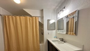 A bathroom with a shower curtain, a sink, a mirror, and a light fixture.