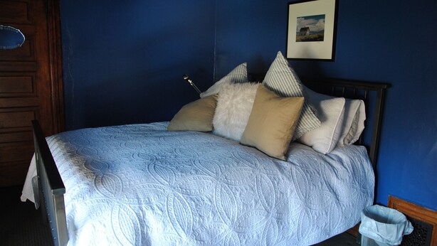 A neatly made bed with a patterned bedspread, a wooden headboard, and a picture on the wall. - Off Broadway B&B (Denver)