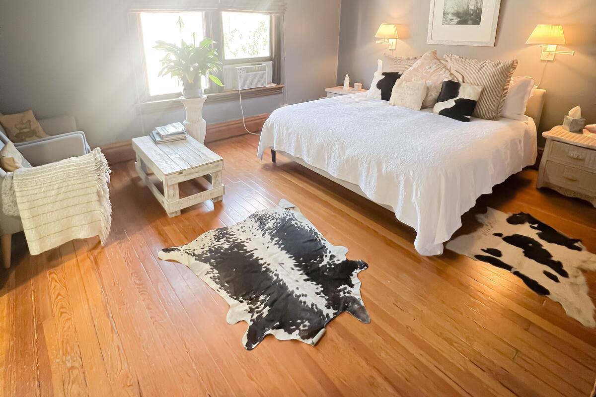 A bedroom with a bed, bedside tables, a ceiling fan, a window, and a cowhide rug.